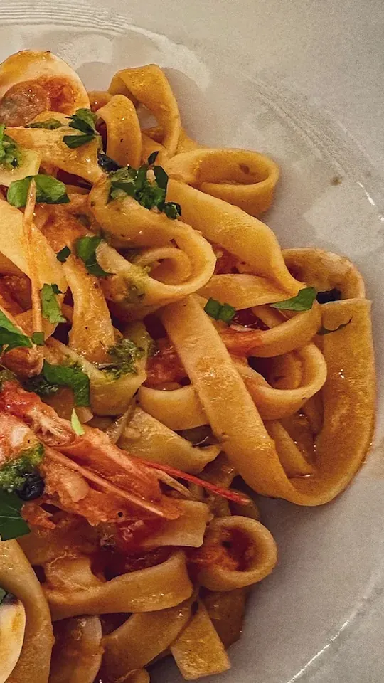 Tagliatelle con gambas enteras con cabeza, almejas abiertas en su concha y perejil picado por encima, de muy cerca en un plato blanco.